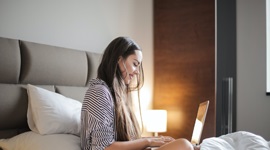 A photo of a beautiful woman sitting in bed while on her laptop